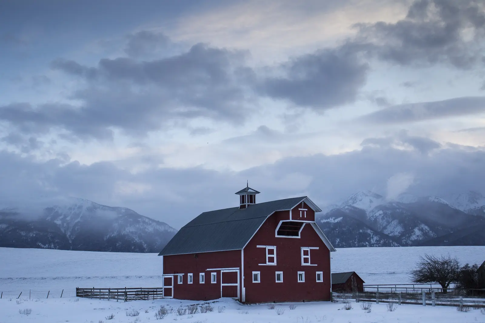 Red barn standing in a snowy field below the mountains