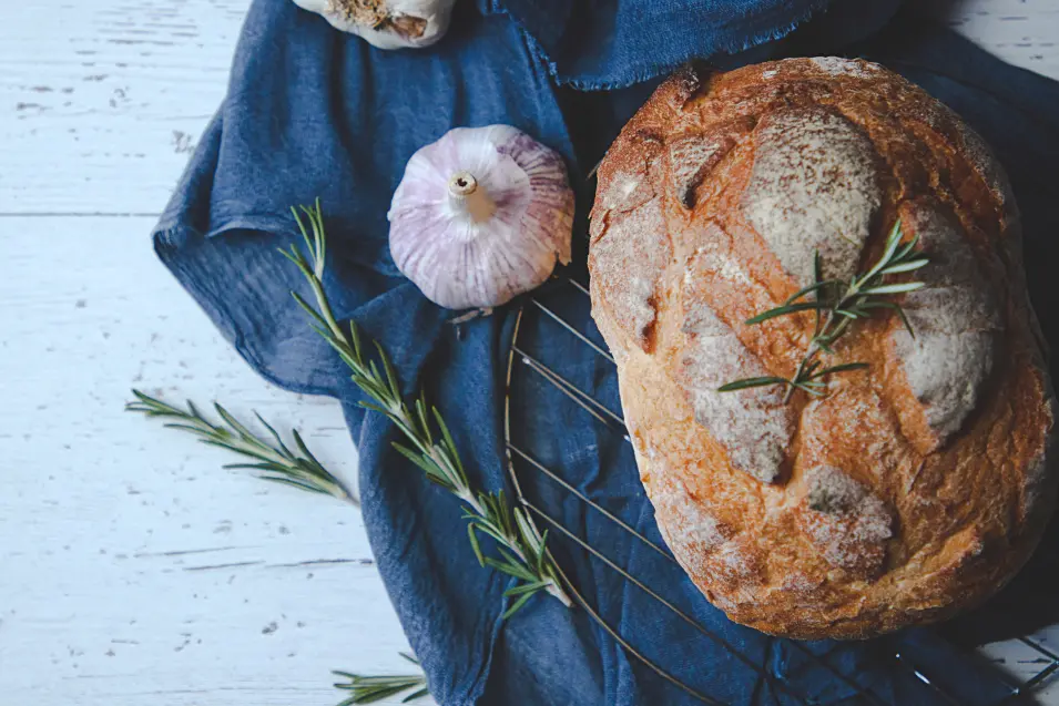 Rustic round loaf of bread with rosemary on blue linen