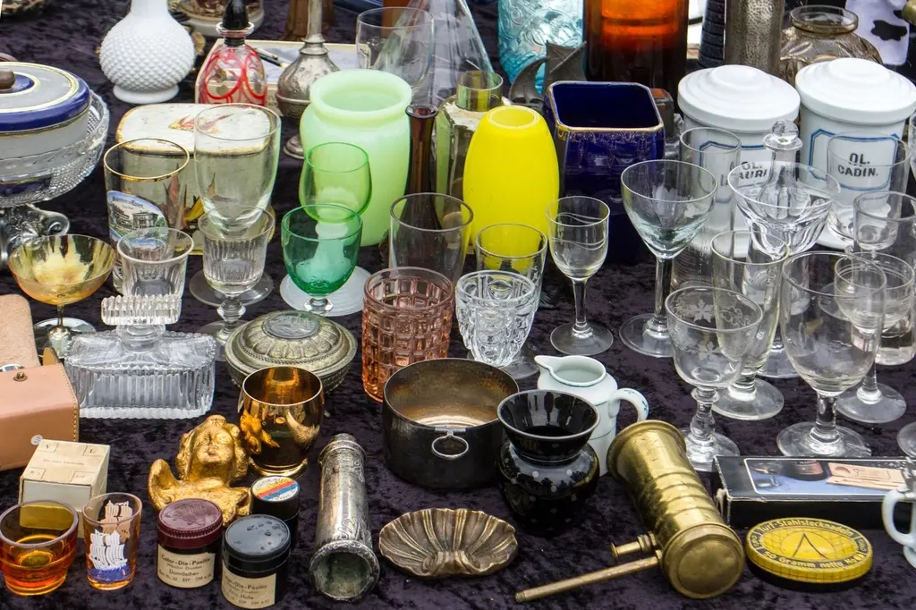 Flea market table covered with vintage glassware, colored bottles and brass pieces