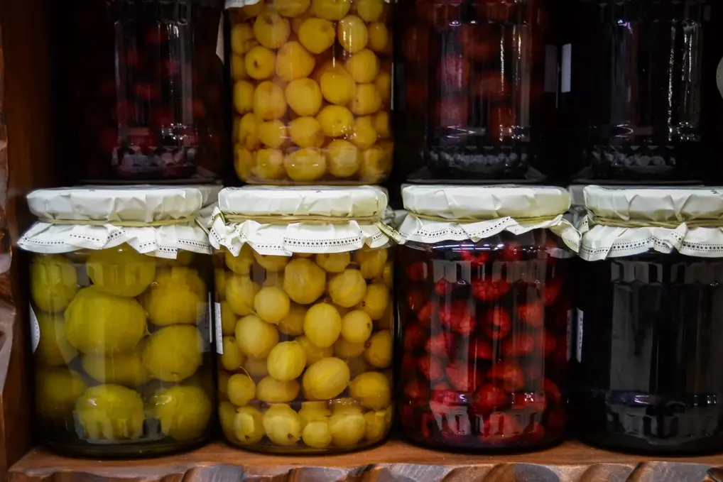 Shelves of home-canned lemons and cherries in jars with cloth-topped lids